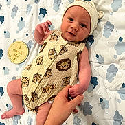 Leo joined the competition — help win amazing prizes! baby, infant, child, hand, blanket, pattern, animal_print, onesie, hat, milestone, wooden_disk, cloud_pattern, skin, cute, holding_hand, lying_down, indoors, soft_lighting, smiling, person