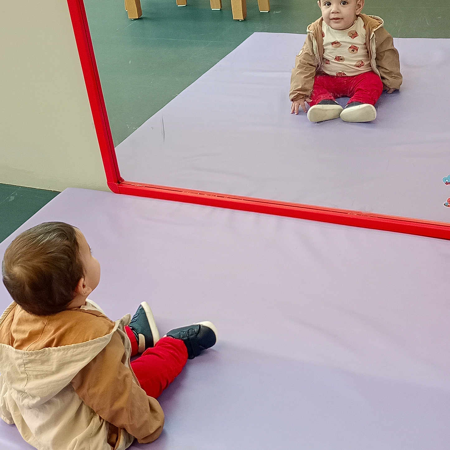 Saif participe au concours pour gagner de l'argent avec cette photo : casual_clothing, child, curious, expression, floor, indoor, jacket, looking, mirror, playroom, purple_mat, red_frame, red_pants, reflection, reflection_image, seated, shoes, toddler, wooden_chair, young_child