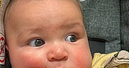 Noah is registered to the contest to win money with this photo: baby, infant, child, portrait, stroller, seated, face, eyes, hands, finger, smiling, curious, indoors, clothing, yellow, animal_print, fabric, close_up, photography, safe
