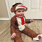 Andrew is registered to the contest to win money with this photo: toddler, child, monkey_costume, hat, red_scarf, smile, sitting, floor, tile_floor, indoor, cute, face, clothing, costume, playful, baby, person, happy, funny, portrait