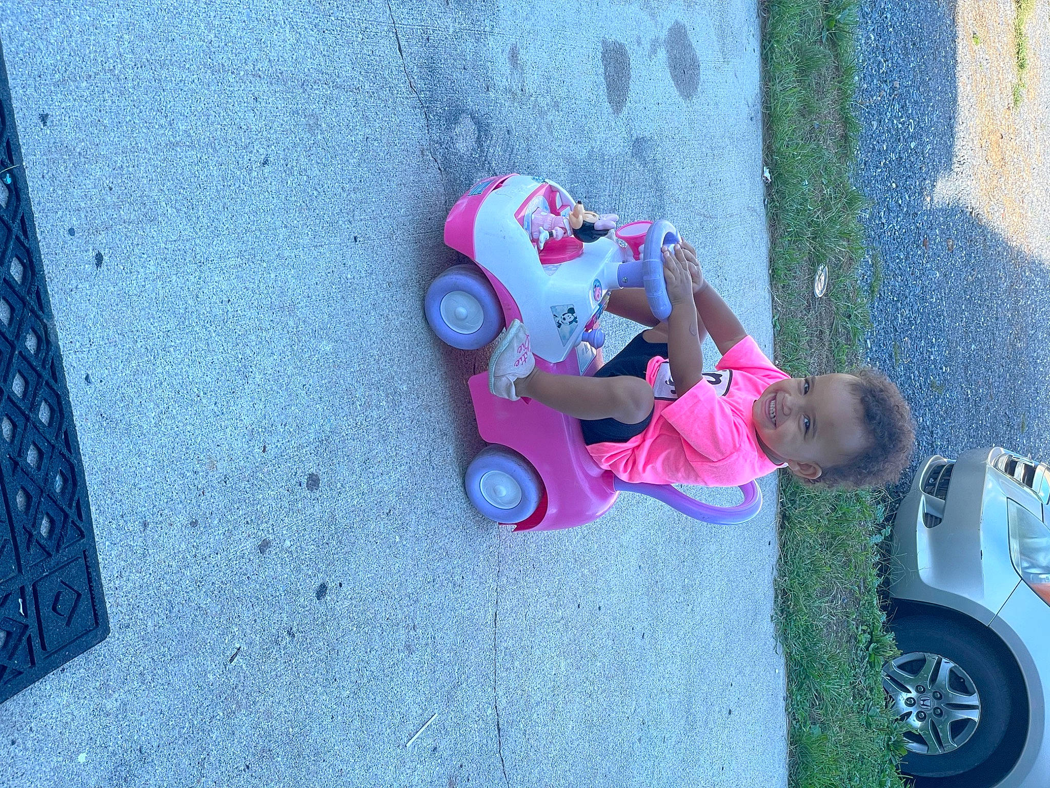 Cali is registered to the contest to win money with this photo: asphalt, automotive_design, automotive_exterior, blue, car, fun, grass, jeans, joy, motor_vehicle, person, pink, plant, public_space, shoe, sidewalk, tire, toddler, vehicle, vehicle_door