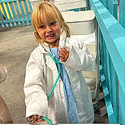 Marceline is registered to the contest to win money with this photo: child, girl, toddler, stethoscope, white_coat, pretend_play, toy, playroom, blue_dress, blond_hair, smiling, indoor, fence, cart, table, happy, portrait, roleplay, clinic, medical_toy