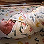 Marcus is registered to the contest to win money with this photo: newborn, baby, swaddled, blanket, footprints, hat, sleeping, hospital, bassinet, infant, cute, soft_lighting, peaceful, wrapped, bed, person, child, resting, cozy, portrait