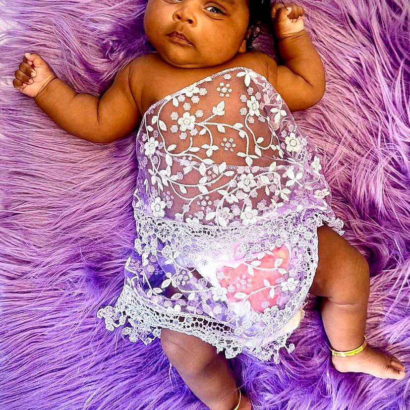 Niyathi is registered to the contest to win money with this photo: adorable, anklet, baby, barefoot, child, cute, decorative_cloth, flower, headband, indoors, infant, lace_clothing, lying_down, peaceful, portrait, purple_rug, skin, small_feet, small_hands, soft_texture