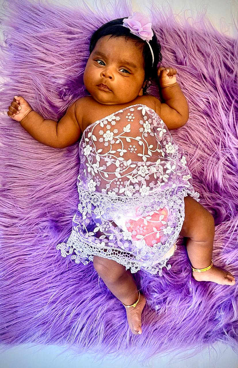 Niyathi is registered to the contest to win money with this photo: baby, infant, purple_rug, lace_clothing, headband, flower, anklet, barefoot, cute, portrait, soft_texture, lying_down, indoors, child, adorable, skin, small_hands, small_feet, decorative_cloth, peaceful