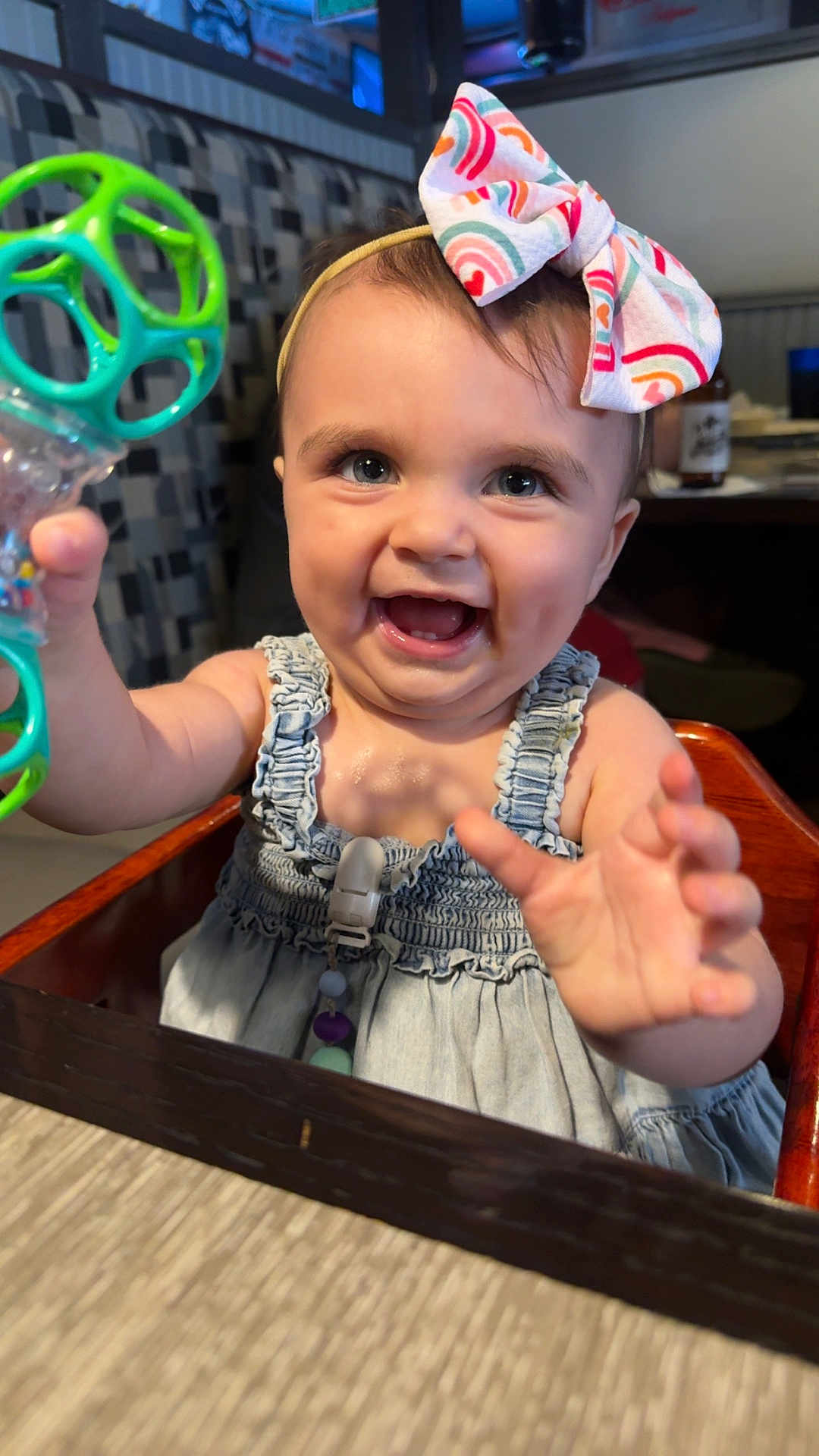 Scarlett is registered to the contest to win money with this photo: baby, child, smiling, happy, toy, high_chair, bow, headband, clothing, indoor, person, table, furniture, skin, face, hand, blue_eyes, dress, cute, cheerful