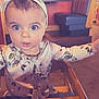 Scarlett is registered to the contest to win money with this photo: baby, child, high_chair, headband, floral_pattern, restaurant, wooden_furniture, curious, wide_eyes, seated, indoor, portrait, clothing, face, person, cute, infant, table, background, decor
