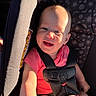 arm, baby, car_seat, child, cute, happy, head, indoors, infant, person, pink_clothing, safety_harness, seat, seatbelt, shadow, skin, smiling, sunlight, warning_label, young_child