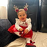baby, child, smiling, red_dress, white_tights, red_shoes, reindeer_antlers, headband, black_chair, blanket, pillow, indoors, cute, holiday, festive, happy, sitting, person, portrait, cozy