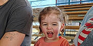 Freyja joined the competition — help win amazing prizes! child, laughing, curly_hair, orange_shirt, cartoon_character, bleachers, outdoor, daylight, people, casual_clothing, tattoo, hat, hand, smiling, portrait, bench, spectator, family, fun, event