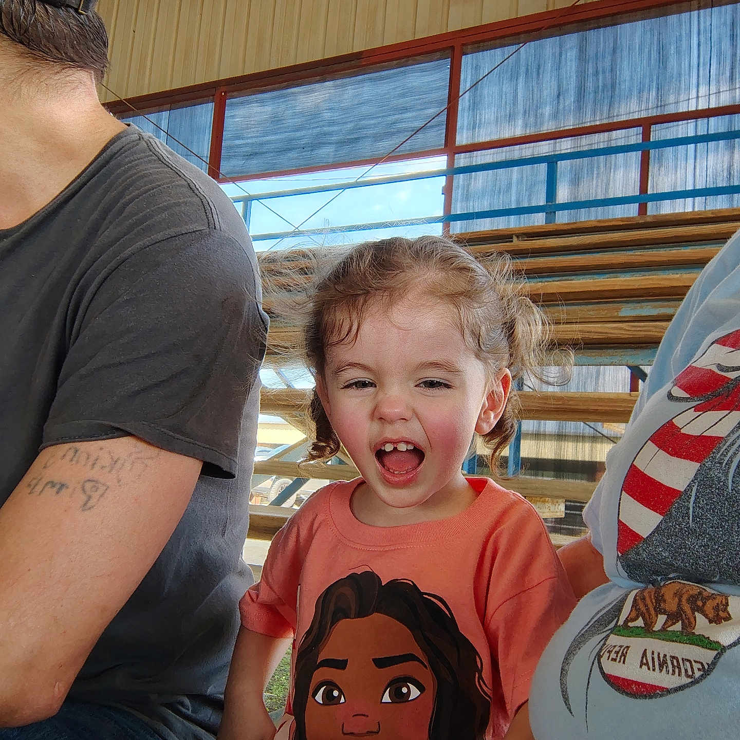 Freyja joined the competition — help win amazing prizes! bench, bleachers, cartoon_character, casual_clothing, child, curly_hair, daylight, event, family, fun, hand, hat, laughing, orange_shirt, outdoor, people, portrait, smiling, spectator, tattoo