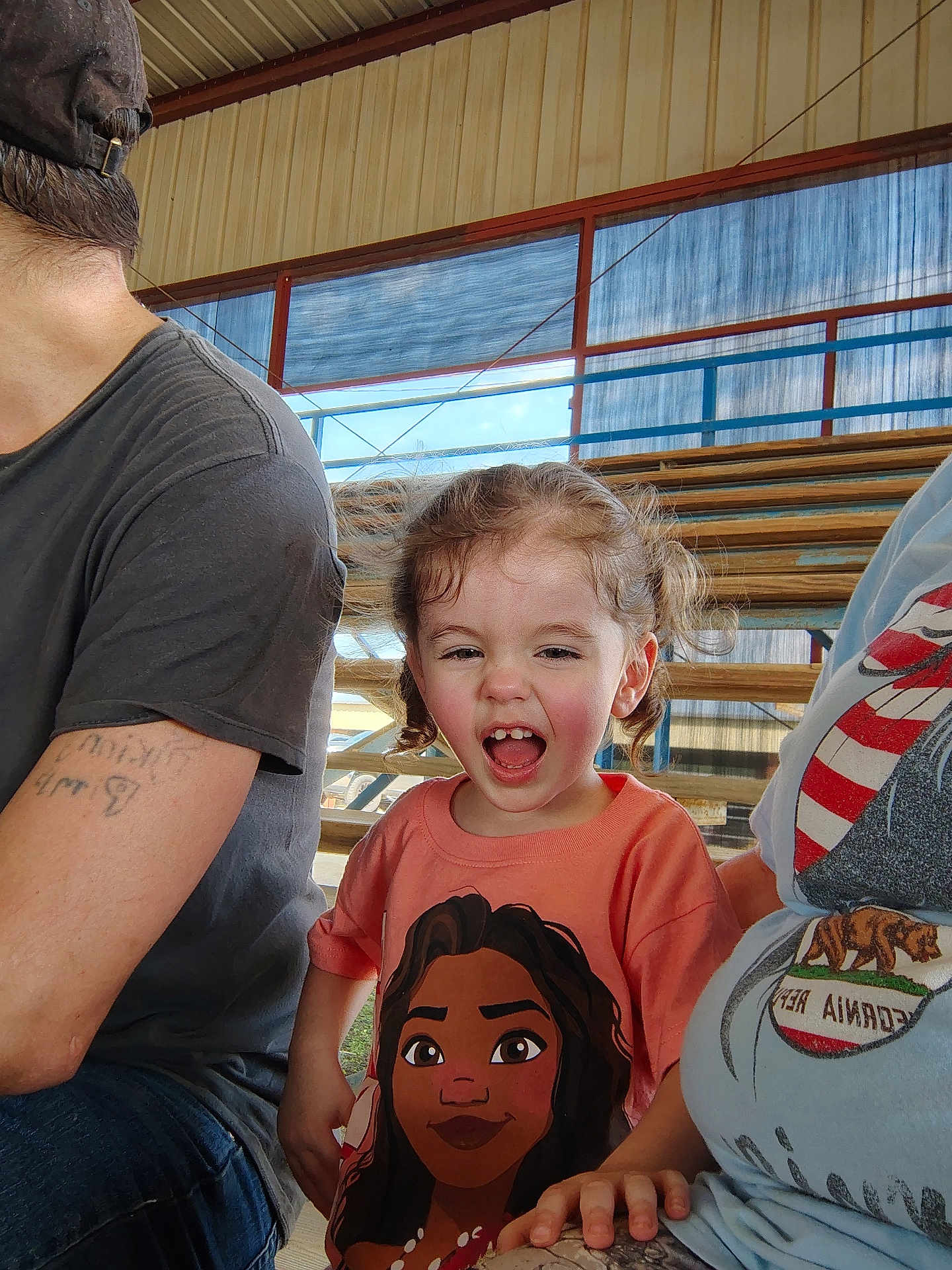 Freyja joined the competition — help win amazing prizes! child, laughing, curly_hair, orange_shirt, cartoon_character, bleachers, outdoor, daylight, people, casual_clothing, tattoo, hat, hand, smiling, portrait, bench, spectator, family, fun, event