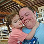 Freyja joined the competition — help win amazing prizes! child, adult, hug, closeup, indoor, casual_clothing, curly_hair, smile, affection, person, portrait, light, metal_roof, barn, fence, red_shirt, blue_shirt, skin, happy, family