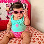 baby, child, sunglasses, pigtails, turquoise_top, pink_shorts, cushion, floral_pattern, minnie_mouse, indoor, cute, portrait, toddler, fashion, accessory, wall, seated, hand, foot, pacifier