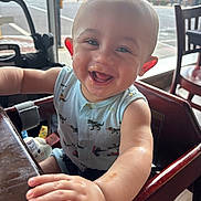 Cassian joined the competition — help win amazing prizes! baby, high_chair, smiling, messy_face, indoor, restaurant, table, arm, clothing, person, child, happy, seat, window, street, toy, wood, daylight, face, expression