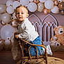 Léo participe au concours pour gagner de l'argent avec cette photo : toddler, child, chair, wicker, balloons, white, bronze, decor, teddy_bear, stuffed_animal, floor_rug, wooden_floor, portrait, indoor, cute, happy, clothing, sneakers, smile, baby