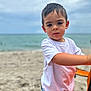 child, boy, beach, ocean, sand, white_tshirt, shorts, curious, outdoor, summer, playing, young, person, nature, sky, water, vacation, fun, casual, exploring