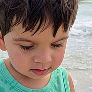 Caleb is registered to the contest to win money with this photo: child, boy, portrait, close_up, face, hair, eyelashes, green_shirt, beach, ocean, water, summer, outdoor, casual_clothing, young, thoughtful, natural_light, skin, toddler, peaceful