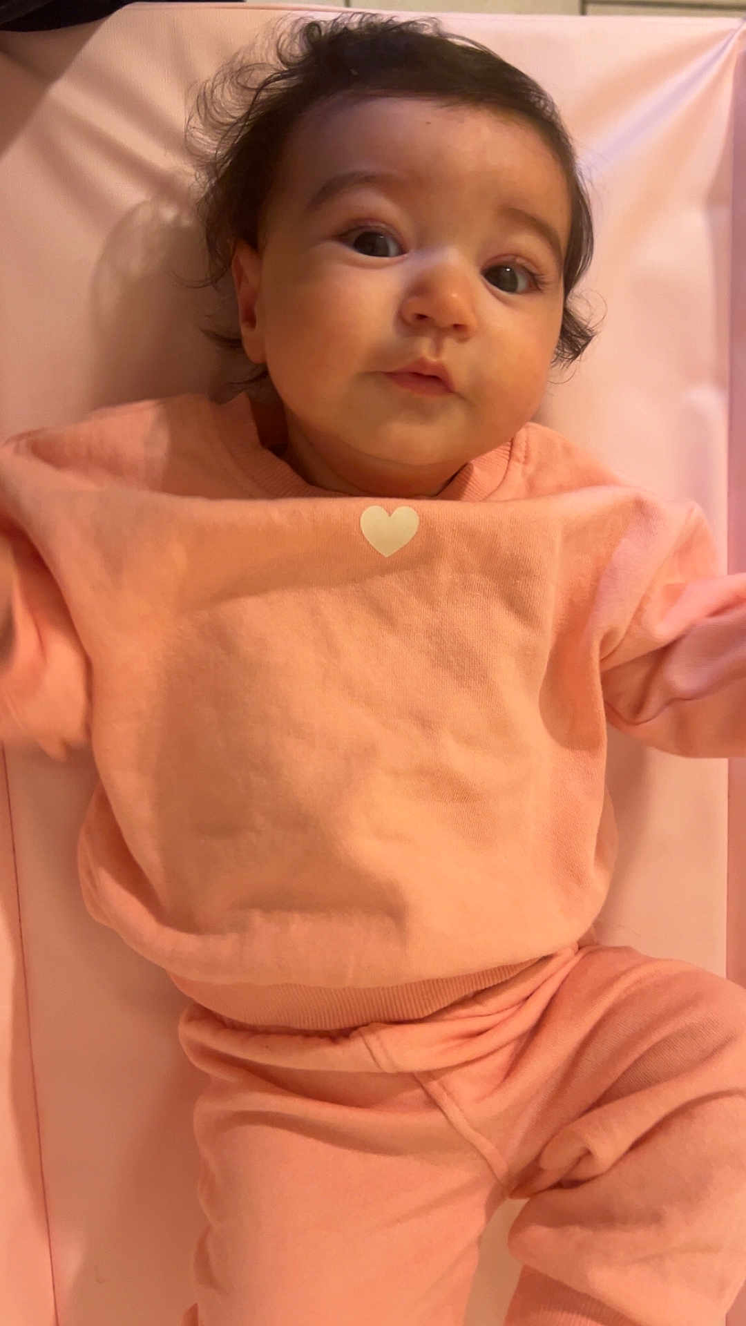 Ambre participe au concours pour gagner de l'argent avec cette photo : baby, infant, pink_clothing, heart_symbol, lying_down, curly_hair, indoors, soft_fabric, cute, portrait, child, person, closeup, expression, skin, face, eyes, mouth, head, cozy