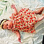 baby, infant, child, floral_dress, headband, lying_down, bed_sheet, patterned, footwear, shoes, skin, cute, small_hands, small_feet, indoors, soft_light, portrait, young_child, colorful_clothing, resting