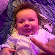 Sebastian joined the competition — help win amazing prizes! baby, infant, smile, face, hand, onesie, blanket, purple, soft_texture, child, cute, lying_down, cozy, happy, indoor, person, skin, finger, expression, young