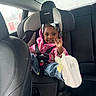 automobile, backseat, black_hair, car_interior, car_seat, casual_clothing, child, cute, footwear, happy, jeans, person, pink_jacket, portrait, safety, seatbelt, sitting, smiling, white_bow, young_child
