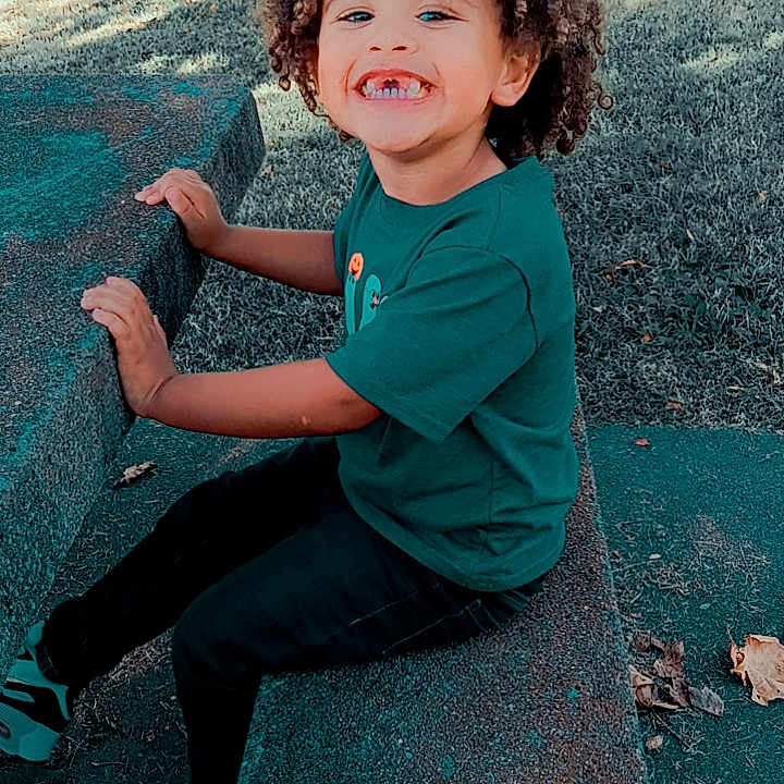 Marcellus is registered to the contest to win money with this photo: boy, child, clothing, face, footwear, hair, happy, head, jeans, male, outdoorplayarea, outdoors, pants, person, photography, playarea, portrait, shoe, sitting, smile