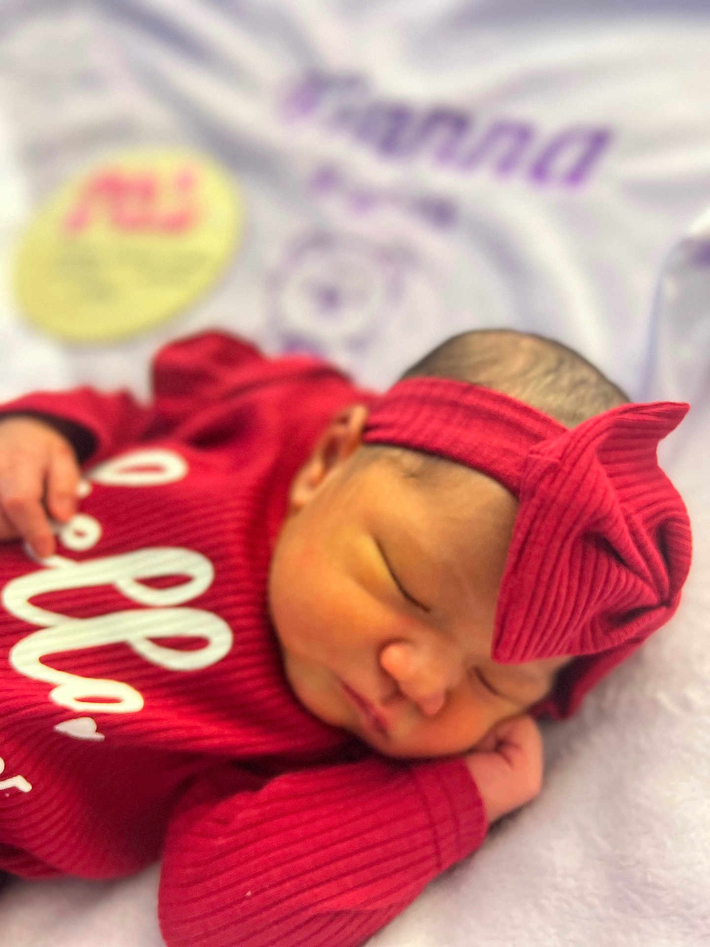 Kianna is registered to the contest to win money with this photo: newborn, baby, sleeping, red_clothing, headband, bow, infant, soft_blanket, closeup, portrait, peaceful, resting, indoors, cute, human, small_hand, face, skin, child, cozy