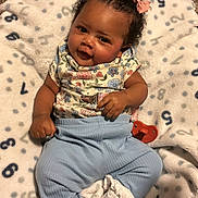 Alayah is registered to the contest to win money with this photo: baby, child, infant, smile, curly_hair, pink_bows, floral_top, blue_pants, white_socks, blanket, numbers, carpet, indoor, cute, happy, portrait, person, lying_down, comfort, cozy