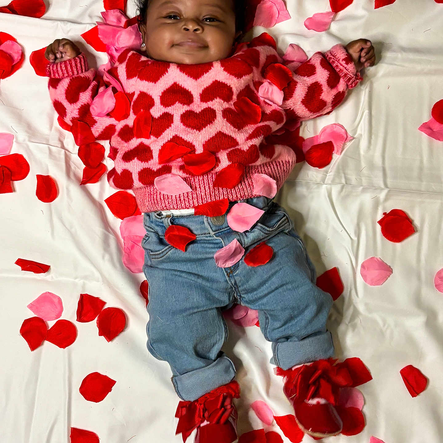 Alayah is registered to the contest to win money with this photo: baby, infant, smiling, heart_pattern, sweater, denim_jeans, red_shoes, rose_petals, white_sheet, lying_down, cute, happy, portrait, child, indoors, clothing, colorful, cozy, playful, adorable
