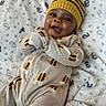 baby, child, smiling, hat, knit_hat, onesie, bee_pattern, blanket, soft_texture, lying_down, happy, cute, infant, portrait, indoor, warm, cozy, face, person, clothing