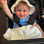 Ella-Rose is registered to the contest to win money with this photo: baby, child, stroller, hat, white_hat, blue_dress, daisies, blanket, smiling, happy, indoor, person, infant, cute, waving, seatbelt, face, legs, black_stroller, joyful