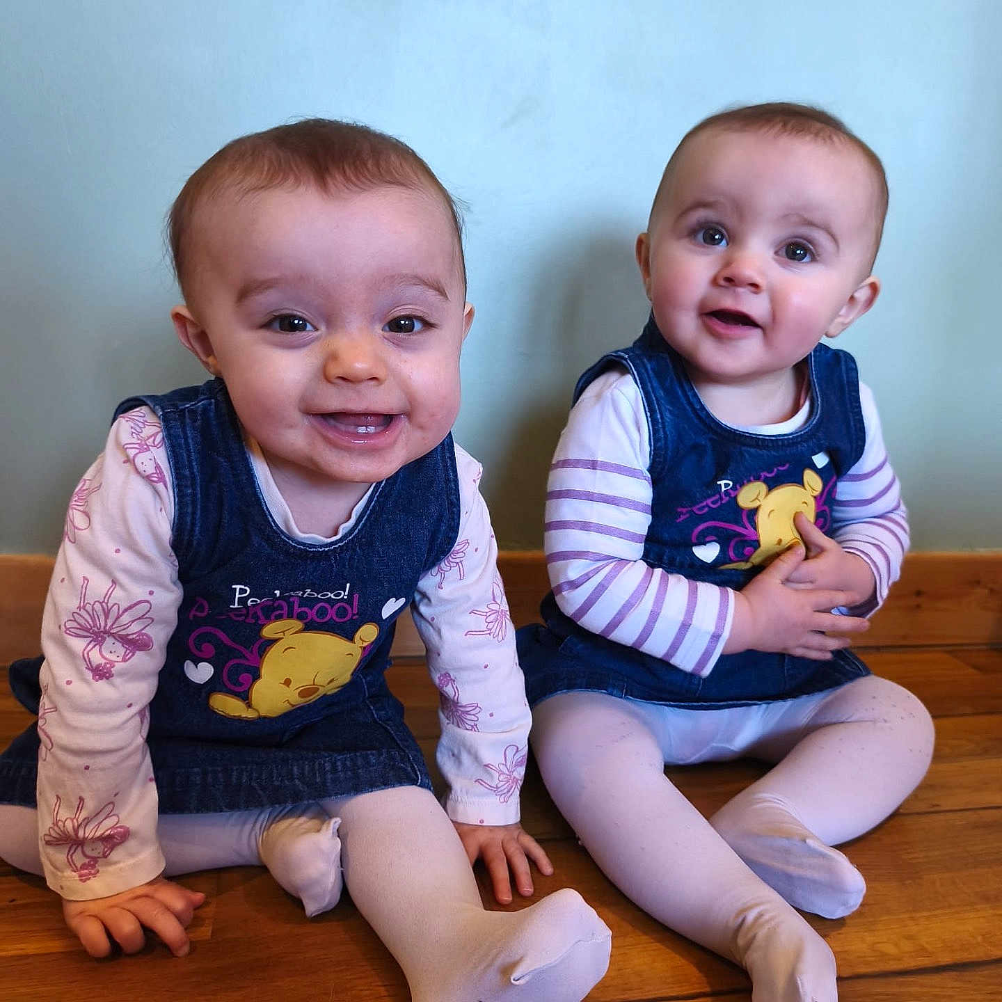 Ilyanna Et Ayanna participe au concours pour gagner de l'argent avec cette photo : baby, infant, toddler, child, denim_dress, white_tights, floor, wooden_floor, sitting, smiling, happy, cute, indoor, two_children, matching_outfits, cartoon_print, long_sleeve_shirt, pink, blue, person
