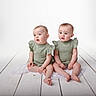 Ilyanna Et Ayanna a rejoint le concours — aidez-le/la à gagner de superbes lots ! babies, baby, child, cloth, curious_expression, cute, floor, floorcloth, green_clothing, indoor, infant, matching_outfits, portrait, sitting, soft_lighting, studio, toddler, two_children, white_background, wooden_floor