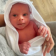 Henry joined the competition — help win amazing prizes! baby, infant, towel, wrapped, hands, face, skin, newborn, wood_floor, person, holding, curious, indoors, soft_texture, white, closeup, child, human, gentle, clean