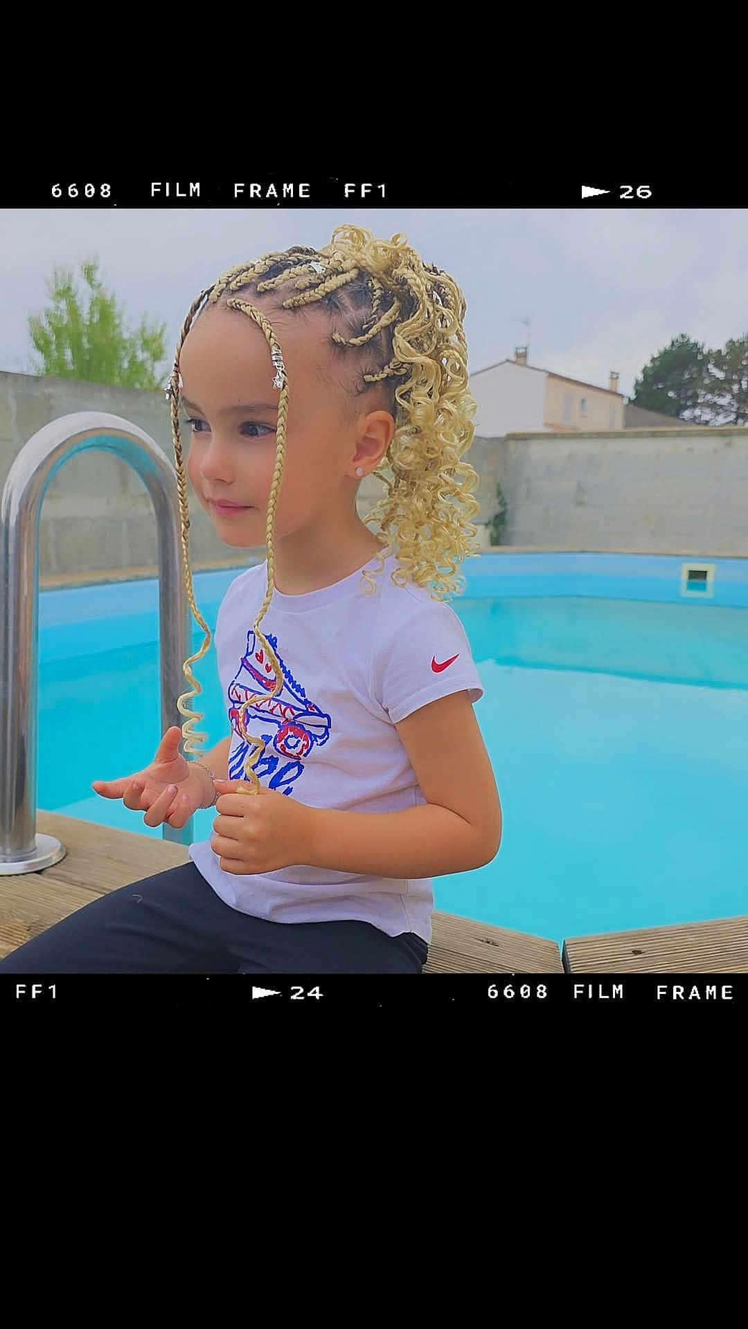 Mila a rejoint le concours — aidez-le/la à gagner de superbes lots ! child, braided_hair, curly_hair, blonde_hair, white_tshirt, nike_logo, pool, outdoor, wooden_deck, casual_clothing, young_girl, earrings, calm, daytime, residential_area, fence, trees, portrait, sitting, fashion
