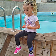 Mila a rejoint le concours — aidez-le/la à gagner de superbes lots ! child, pool, outdoor, braided_hair, pink_sneakers, wooden_structure, concrete_wall, blue_pool, cloudy_sky, casual_clothing, sitting, young_child, thoughtful, residential_area, ladder, sporty, nike, curly_hair, daytime, calm