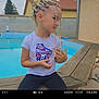 child, braids, pool, outdoor, tshirt, roller_skate, bench, hairstyle, beads, young_girl, casual_clothing, residential, fence, wooden_bench, side_profile, earrings, relaxed, daytime, playful, portrait