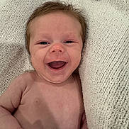 Logan is registered to the contest to win money with this photo: baby, smiling, infant, blanket, knitted_blanket, happy, skin, hand, nail_polish, closeup, face, expression, portrait, lying_down, cute, child, newborn, soft_texture, warm, care