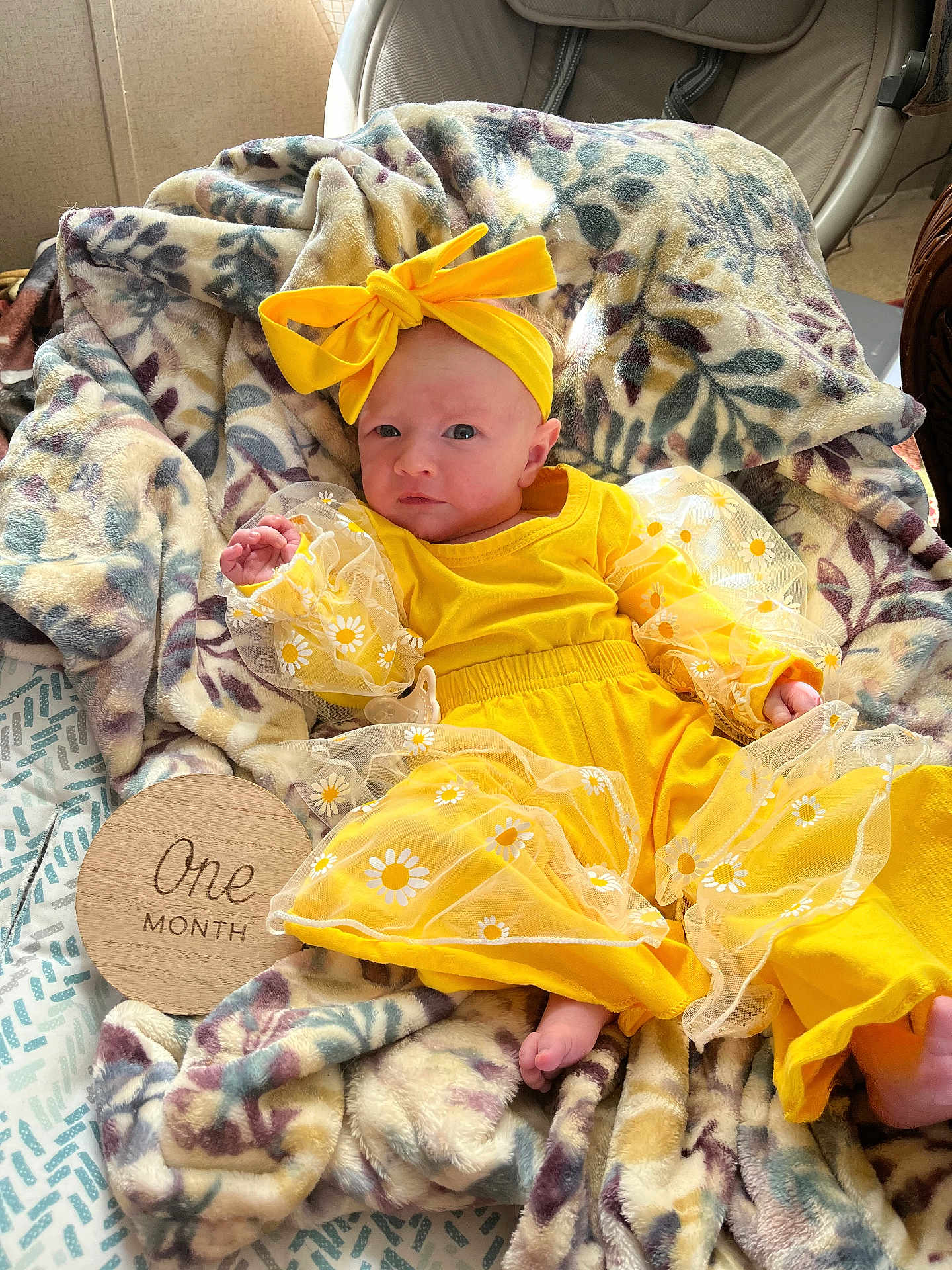 Willow is registered to the contest to win money with this photo: baby, infant, yellow_clothing, headband, bow, blanket, floral_pattern, plush, one_month, milestone, wooden_plaque, cute, newborn, portrait, indoors, soft_texture, baby_boy, baby_girl, clothing, baby_accessories