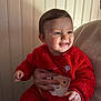 baby, child, smiling, red_clothing, santa_outfit, holiday, person, portrait, indoor, holding_hand, cute, happy, infant, blue_eyes, cozy, warm_lighting, fuzzy_texture, panel_wall, hand, face