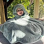 baby, child, hooded_poncho, fluffy, smiling, outdoor, sunlight, wooden_table, greenery, happy, cute, cozy, portrait, infant, face, person, nature, daylight, warm_clothing, covered