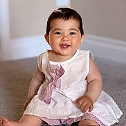 Layla is registered to the contest to win money with this photo: baby, child, smiling, dress, hair_clip, indoors, carpet, sitting, cute, happy, portrait, pink, white, infant, person, toddler, skin, feet, clothing, young
