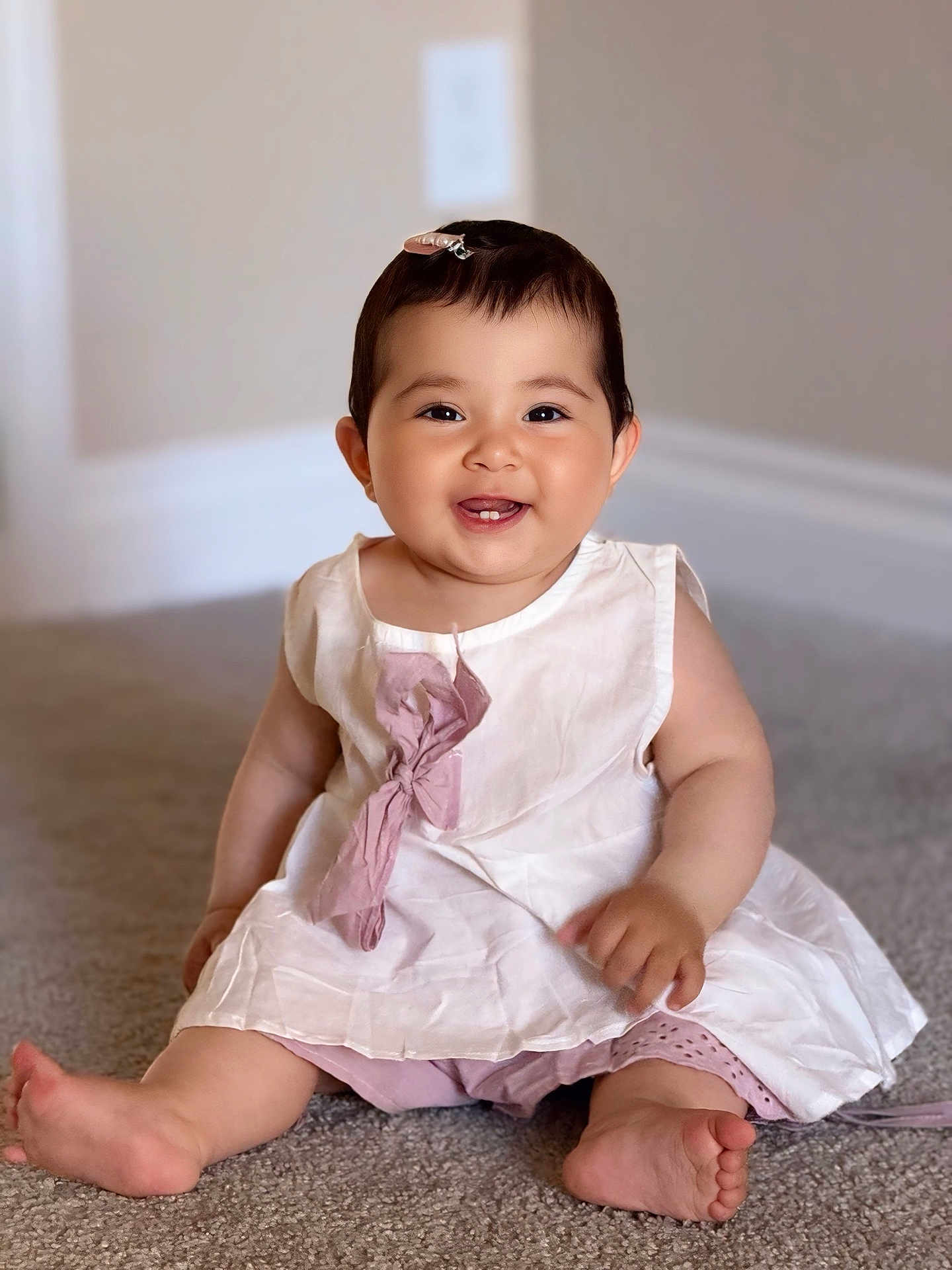 Layla is registered to the contest to win money with this photo: baby, child, smiling, dress, hair_clip, indoors, carpet, sitting, cute, happy, portrait, pink, white, infant, person, toddler, skin, feet, clothing, young