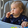 Jules participe au concours pour gagner de l'argent avec cette photo : toddler, child, high_chair, cracker, toy, piano_toy, indoor, window, blue_clothing, space_pattern, hand, face, blond_hair, light, food, snack, curious, seated, baby, portrait
