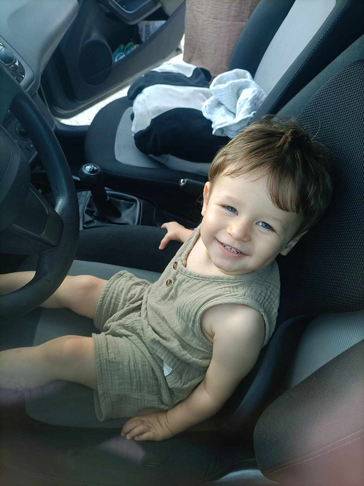 Owenn participe au concours pour gagner de l'argent avec cette photo : baby, blanket, blue_eyes, car_interior, casual, child, clothing, driver_seat, fabric, hair, happy, indoor, person, seat, seatbelt, shorts, sleeveless_shirt, smiling, steering_wheel, toddler