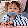 baby, blue_eyes, child, closeup, curious, cute, daylight, face, floral_pattern, hands, hat, jacket, outdoor, pacifier, person, resting, striped_clothing, sunlight, toddler, young_child