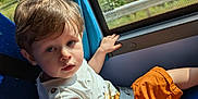 Owenn a rejoint le concours — aidez-le/la à gagner de superbes lots ! bus_seat, casual_clothing, child, curtain, daylight, face, hair, hand, indoor, nature_outside, orange_shorts, person, portrait, seat, seatbelt, sunlight, toddler, travel, white_shirt, window