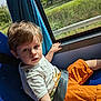 bus_seat, casual_clothing, child, curtain, daylight, face, hair, hand, indoor, nature_outside, orange_shorts, person, portrait, seat, seatbelt, sunlight, toddler, travel, white_shirt, window