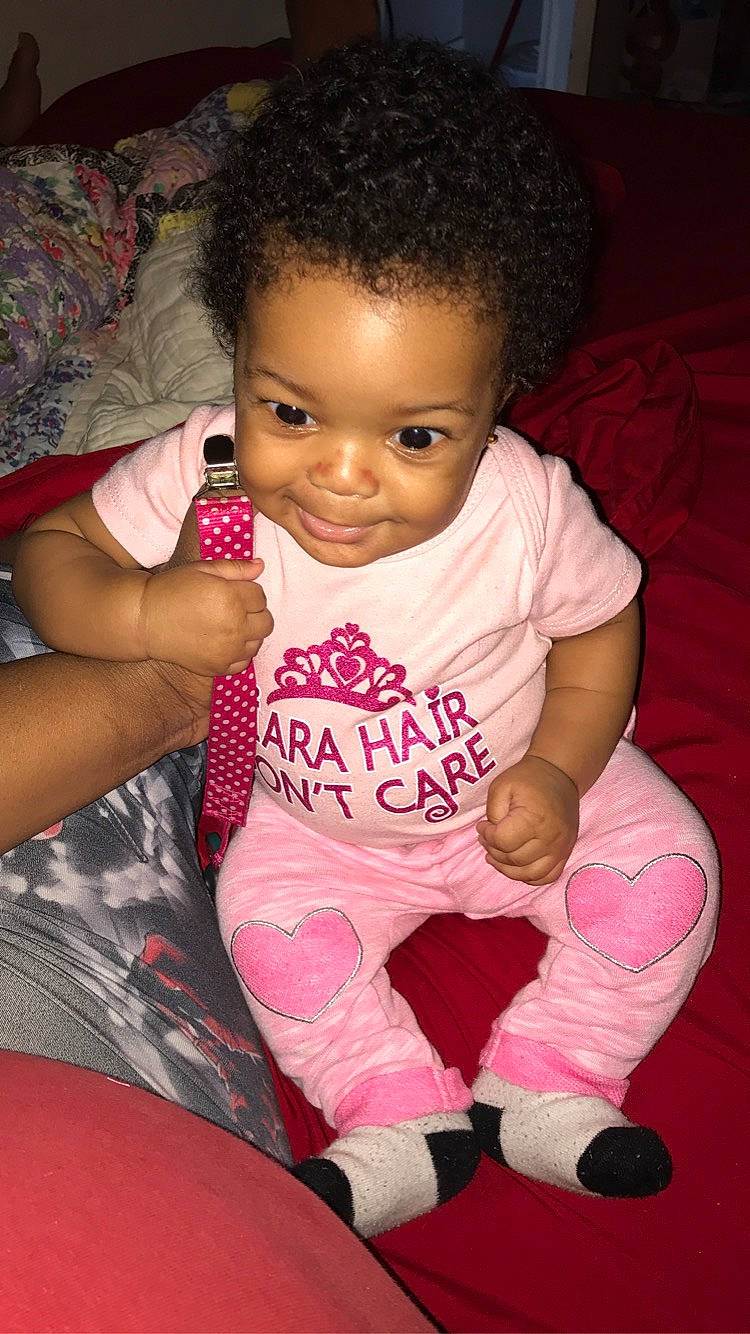 Isabella is registered to the contest to win money with this photo: arm, baby, black_hair, cheek, child, eye, finger, joy, leg, lip, mouth, person, pink, sitting, skin, smile, thigh, thumb, toddler